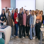 На групповом фото запечатлена большая компания людей, преимущественно женщин, позирующих в современном учебном или выставочном пространстве.  На заднем плане виден большой экран с логотипом «ЗДРАВ», а некоторые участники группы держат в руках сертификаты или папки, что указывает на завершение какого-то образовательного или профессионального мероприятия.