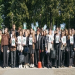 На изображении группа людей стоит на улице, держа в руках белые листы с текстом ФАРМАЦИЯ. Вокруг деревья и зелень.