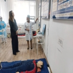 На изображении комната с двумя людьми, один из которых в медицинской форме. На полу лежит манекен.